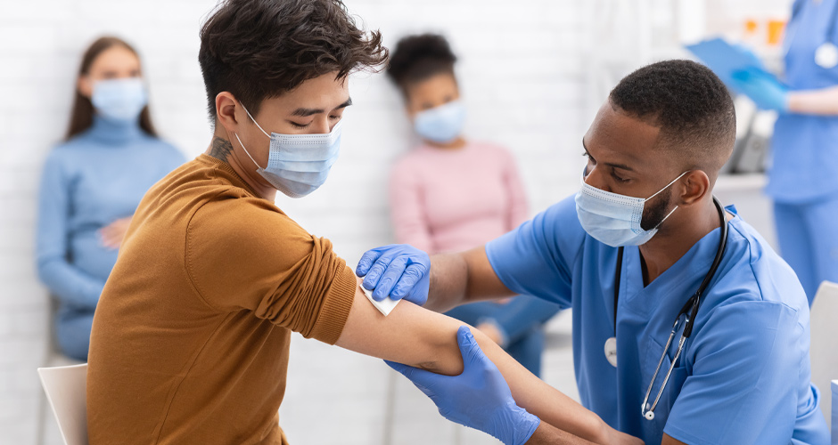 A male nurse cleaning a man's arm to receive a vaccine. Both men are wearing masks.